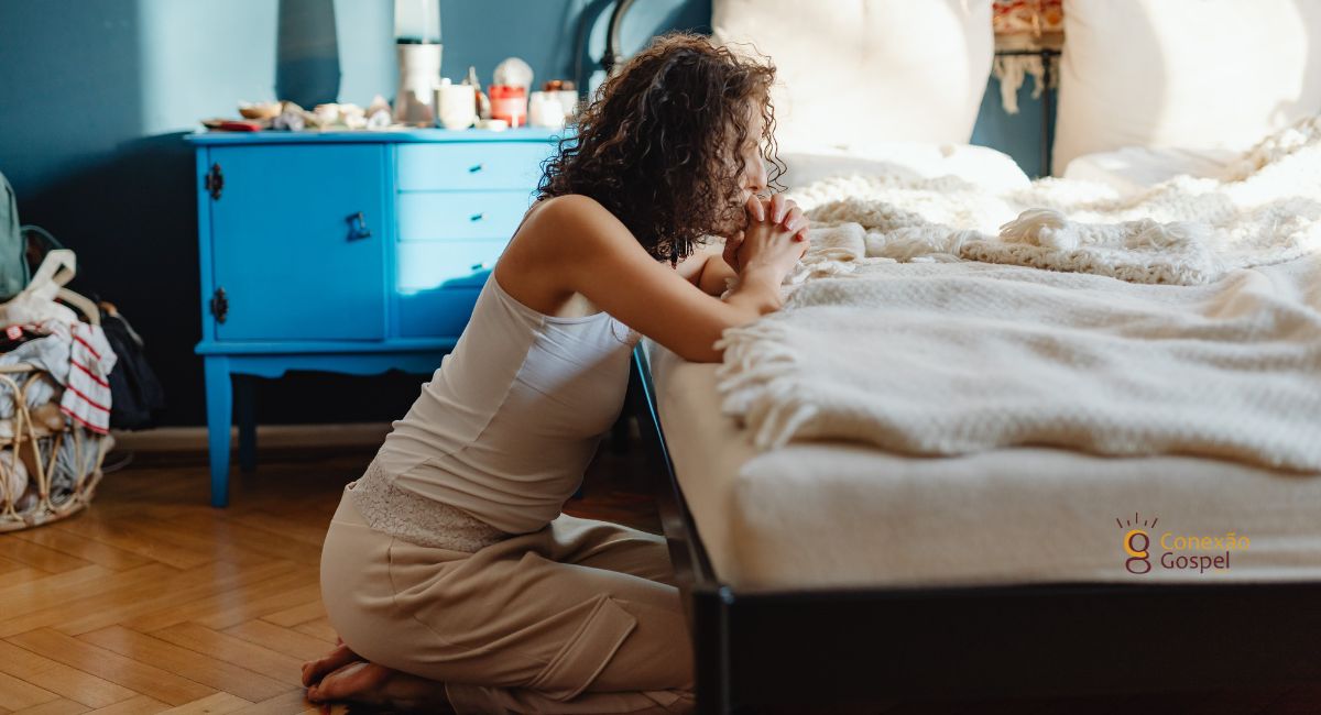 Mulher orando de joelhos no quarto perto da cama. Deus Age Através Da Oração